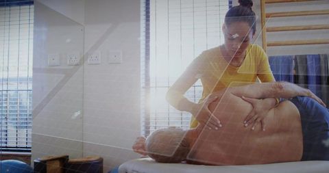 Physiotherapist mobilizing male patient during manual shoulder therapy in sunlit clinic