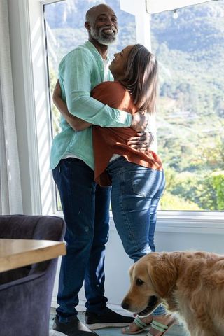 Mature couple embracing at window with golden retriever and scenic valley view