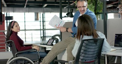 Inclusive team collaborating over charts and laptops in modern open-plan office