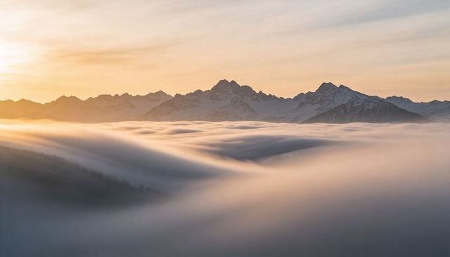 Sunrise fog rolling through alpine valley with snow-dusted peaks
