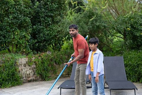 Father and son skimming pool together in backyard