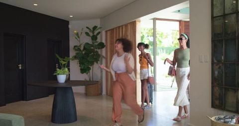 African american friends walking into modern foyer pulling wheeled luggage and carrying handbags