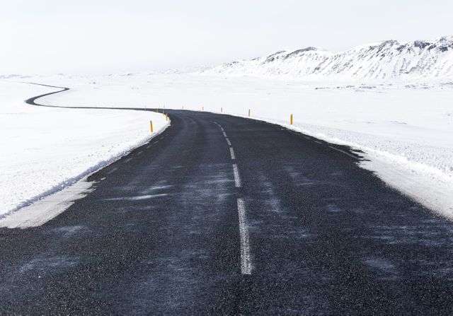 Long, winding road cutting through snowy winter landscape, black asphalt contrasting with white surroundings. Used for travel blogs, adventure stories, winter tourism promotions, scenic drive inspirations.