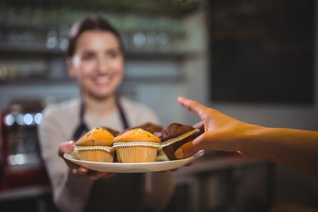 Waitress serving a plate of cupcake to customer in cafÃ©