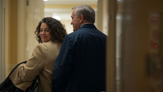 Smiling businesswoman glancing back with colleague in warm office corridor carrying bag