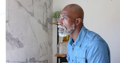 Senior man gazing toward natural light by marble wall in minimal interior, contemplative portrait