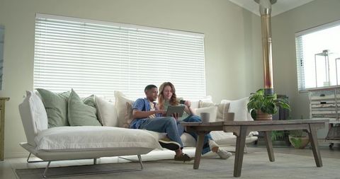Relaxing couple sharing tablet and coffee on white sofa in modern neutral living room