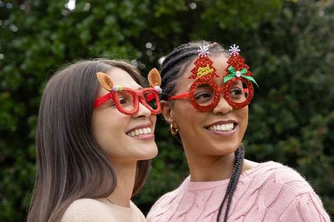 Multicultural friends smiling and wearing festive reindeer and glitter christmas tree glasses