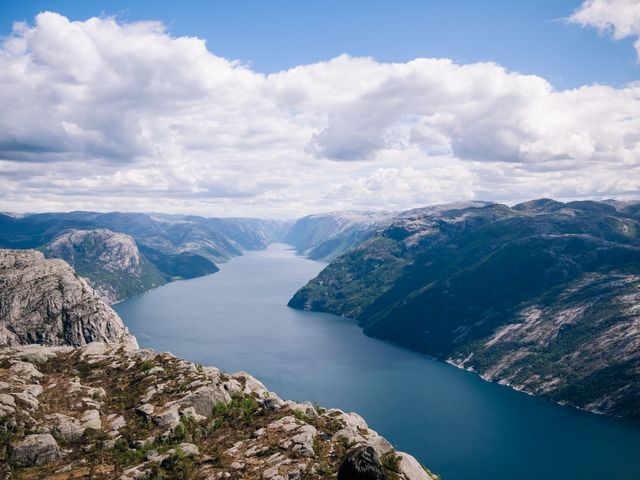 A breathtaking aerial view of a fjord surrounded by rugged, rocky mountains under a beautiful sky with scattered clouds. Ideal for use in travel blogs, nature documentaries, tourism advertisements, and scenic calendars.