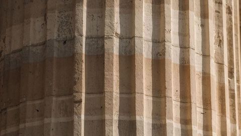 Fluted limestone column showing vertical grooves, weathered patina and shadow bands