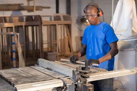 African american carpenter operating table saw in woodshop wearing safety gear