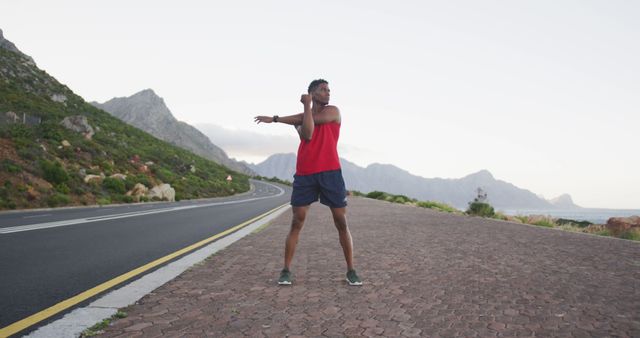 Fitness enthusiast stretching along mountain road during early morning. Suitable for health and fitness campaigns. Ideal for illustrating outdoor workout routines, active lifestyles, and advertisement of athletic apparels.