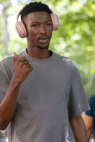 Young african man wearing beige headphones giving thumbs up in park with soft bokeh
