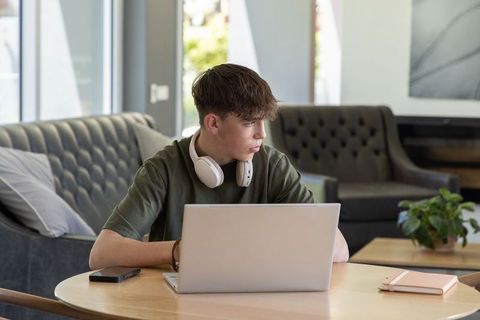 Teen studying on laptop with headphones in sunlit modern lounge for remote learning