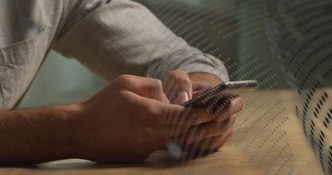Male hands tapping smartphone behind dotted glass partition on wooden cafe table, close-up
