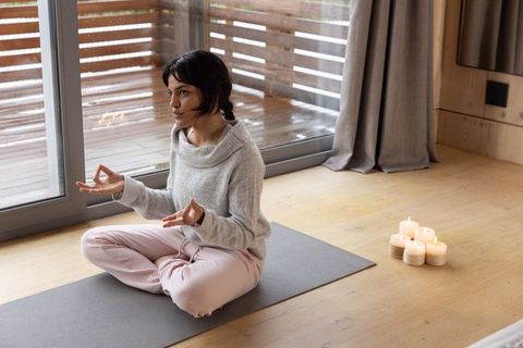 Woman meditating indoors near patio with candlelight and rainy view