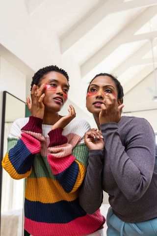 Diverse female friends applying red under-eye patches, enjoying skincare ritual in bright home
