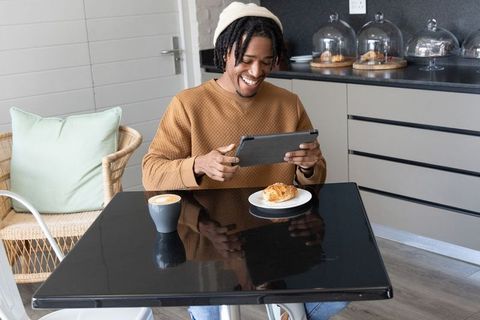 Smiling african american man at cafe enjoying coffee and croissant while using tablet