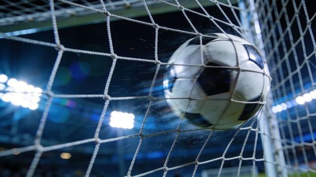 Soccer ball smashing into goal net under stadium floodlights capturing night goal action