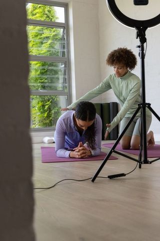 African american trainer guiding client during plank workout in studio with ring light
