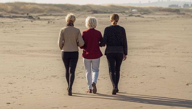 Three women walking linked arms on sunlit sandy beach, seaside companionship and calmness