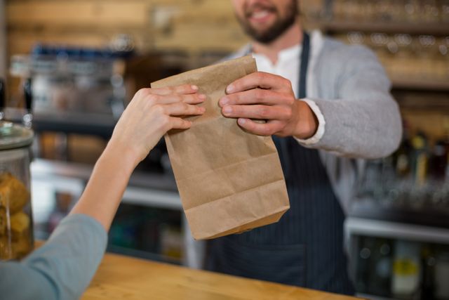 Woman receiving parcel from waiter at counter in cafe
