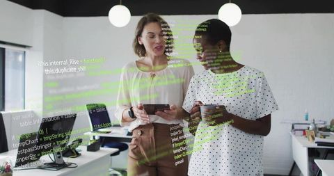 Female developers collaborating on tablet with coffee while reviewing code in modern workspace