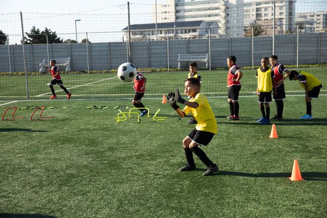 Multi-ethnic boys soccer teams practicing on a green football pitch on a sunny day, running, catching a ball. Childhood healthy lifestyle competition.