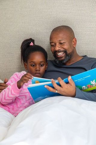 African american father reading bedtime farm animals book with daughter in pink pajamas