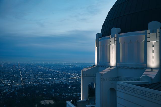 Griffith Observatory is seen illuminated at dusk, with a panoramic view of Los Angeles cityscape below. Ideal for illustrating travel guides, educational materials about astronomy or Los Angeles landmarks, and architectural showcases.