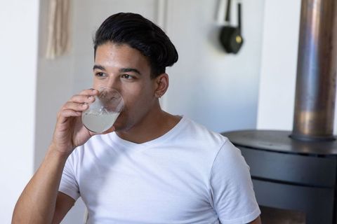 Young african american man sipping icy lemonade in white tee in cozy home kitchen nook