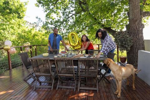 Diverse group setting up outdoor party with balloons and dog on wooden deck