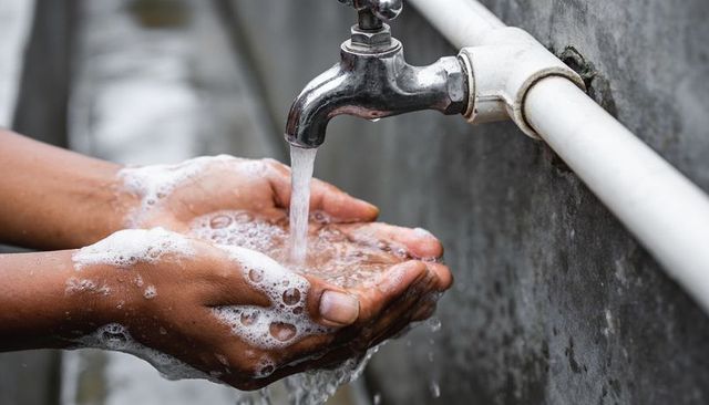 Washing hands under outdoor faucet showing soap lather and flowing water for hygiene