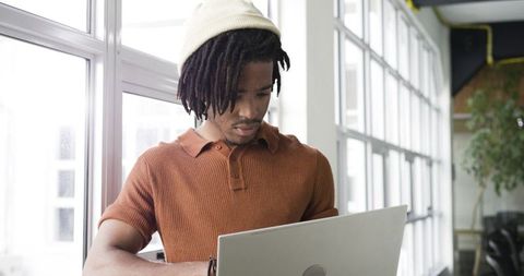 African american man working on laptop by window in bright coworking space