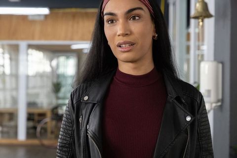 Confident young woman standing in coworking space wearing leather jacket and burgundy top