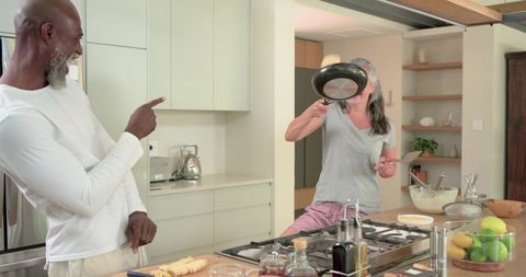 African american couple laughing and flipping pancake while cooking in modern kitchen