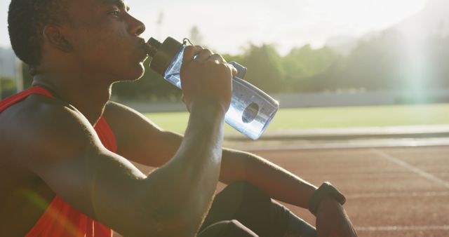 Thoughtful african american male athlete sitting and drinking water at empty stadium - Download Free Stock Photos Pikwizard.com
