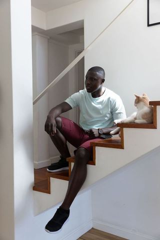Young African American Man Relaxing on Stairs at Home with Cat