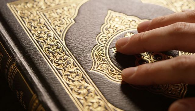 Fingertips pressing ornate gold-embossed leather book cover featuring intricate medallion and border