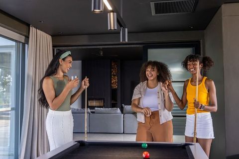 Diverse women laughing and playing pool in modern lounge enjoying casual game night