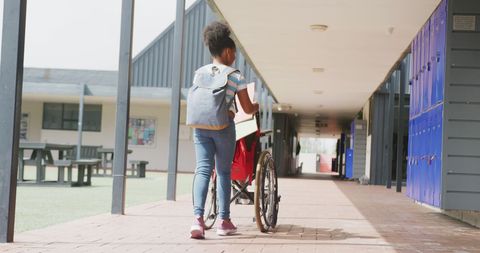 Schoolgirl Pushing Wheelchair in School Corridor