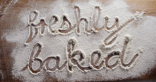 Handwritten 'Freshly Baked' message in flour on rustic wooden table captures the essence of homemade baking. Ideal for use in food blogs, recipe websites, and bakery advertisements.