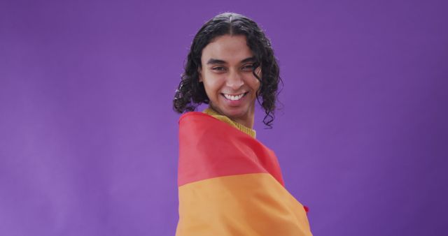 Portrait of happy biracial man holding lgbt flag with arms wide. Spending quality time at home.
