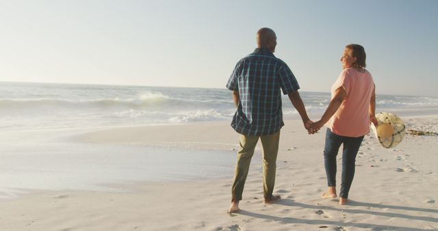 Smiling senior african american couple holding hands and walking on sunny beach - Download Free Stock Photos Pikwizard.com