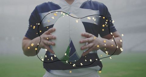 Holding rugby ball closeup, player wearing navy jersey gripping white oval ball on pitch