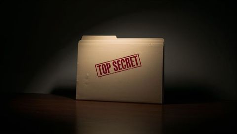 Standing manila folder stamped top secret on wooden desk under dramatic spotlight