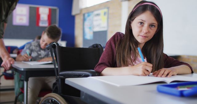 Portrait of happy caucasian schoolgirl sitting in wheelchair in classroom looking at camera. children in primary school