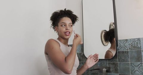 African american woman using facial roller at minimalist bathroom vanity with teal tiles