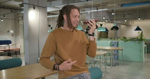 Young African man speaking into smartphone in modern coworking lounge with dreadlocks