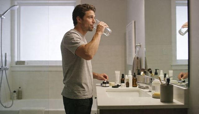 Modern masculine skincare routine: man drinking water while reaching for grooming jar